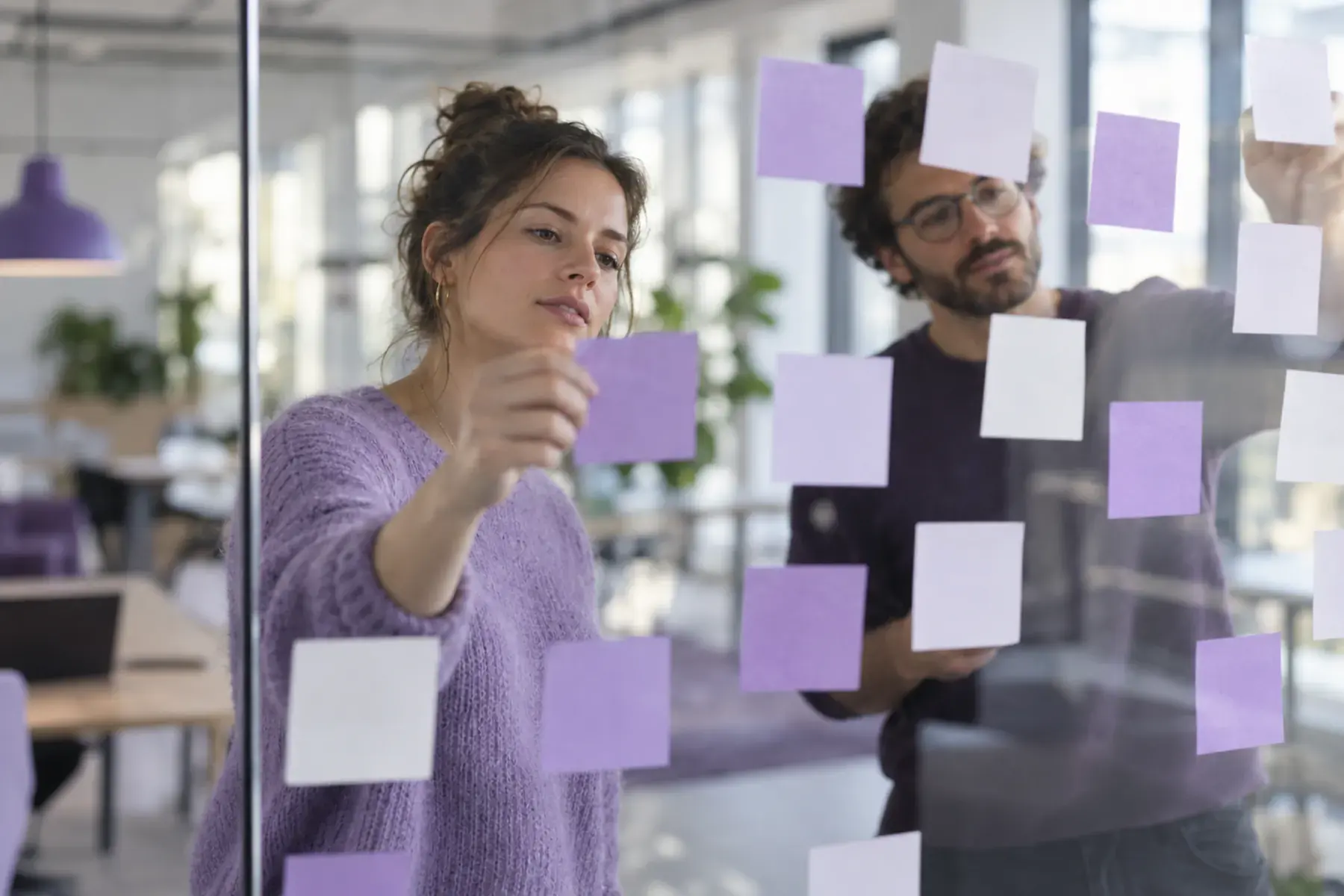 Des post-it lavande sur un mur vitré, lors d’un atelier d’équipe.